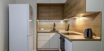 Встроенная угловая кухня под дерево с низом белого цвета со скрытыми ручками на заказ